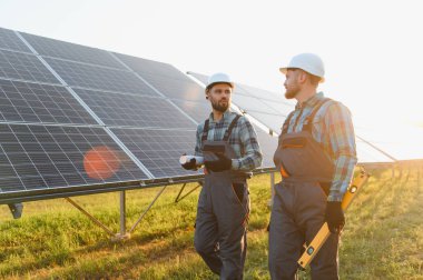 Gün batımında güneş paneli alanında yenilenebilir enerji gelişimini temsil eden planlarını tartışan iki işçi.