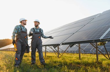 Güneş çiftliğinde yürüyen ve tartışan iki mühendis, temiz elektrik enerjisi üretiyorlar.