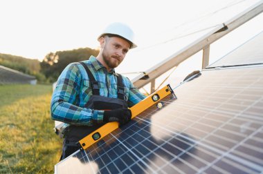 Güneş enerjisi panelleri kuran teknisyen, güneşli bir günde ruh seviyesindeki bir araçla hizalamayı kontrol ediyor