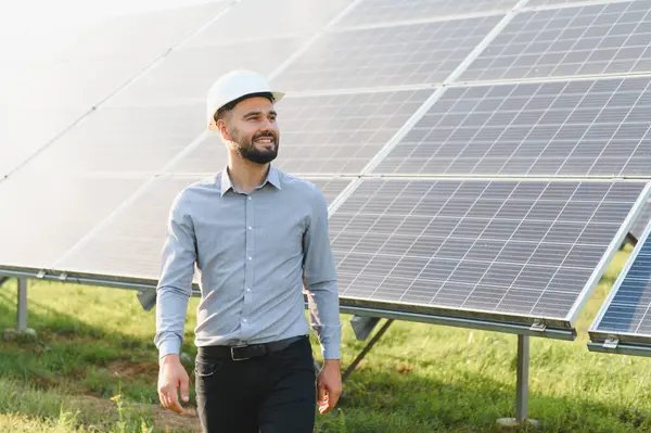 Kemerli şapka takan ve gözünü kaçıran adam, temiz ve sürdürülebilir enerji sağlayan güneş panellerini inceliyor.