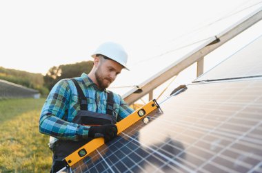 Kask takan ve ekose gömlek giyen erkek teknisyen bir güneş paneli kuruyor ve temiz yeşil enerji üretiyor.