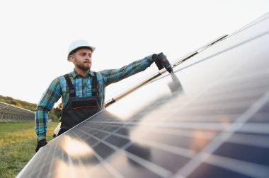 Servis elemanı matkap kullanarak fotovoltaik paneller kuruyor. Bir güneş çiftliğinde yenilenebilir enerji teknolojisi geliştirmek