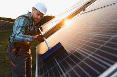 Enerji üretim sistemlerini koruyan işçiler, optimum yenilenebilir enerji üretimini sağlıyorlar. Güneş panelin üzerinde batıyor