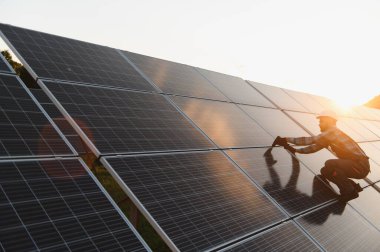 Mühendis fotovoltaik paneller kuruyor, güneş enerjisinden faydalanıyor, günbatımında sürdürülebilir yenilenebilir enerji hedeflerine katkıda bulunuyor
