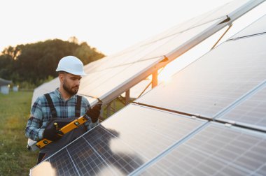 Bir güneş çiftliğine fotovoltaik paneller kuran sabit şapka ve tulum mühendisi, sürdürülebilir temiz enerji üretimi için düzeyi ayarlıyor