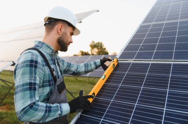 Güvenlik kaskı ve eldiven takan mühendis bir güç istasyonuna güneş panelleri kuruyor ve temiz enerji üretiyor.