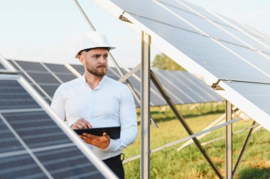 Elinde tablet olan genç mühendis fotovoltaik panelleri kontrol ederek temiz yenilenebilir enerji üretiyor.