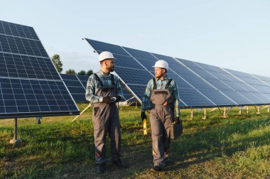 Büyük bir güneş enerjisi santralinde çalışan iki mühendis, panel kurulumunu tartışıyor.