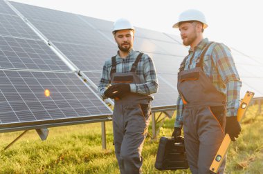 İki güneş enerjisi teknisyeni büyük bir güneş paneli santralinde çalışarak yenilenebilir enerji yüklüyorlar.
