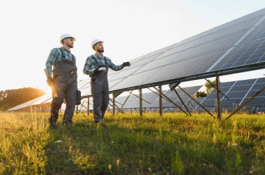 Güneş panellerini inceleyen, büyük bir güneş enerjisi santralinde temiz enerji üretimi sağlayan iki işçi.