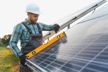 Sert şapkalı ve tulumlu teknisyen güneş panelleri kuruyor, ruh seviyesindeki bir aletle uygun hizayı sağlıyor