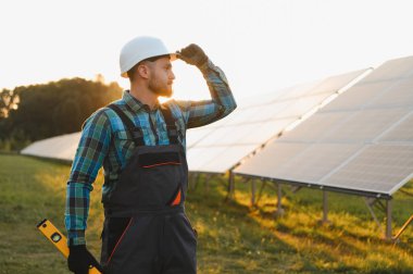Yeşil alandaki güneş panellerine bakarken, yenilenebilir enerji ve sürdürülebilir kalkınma üzerine odaklanan teknisyen gölgeleme gözleri