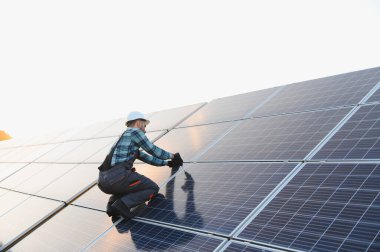 Teknisyen güneş panelinde diz çöküp fotovoltaik hücreleri yenilenebilir elektrik üretmek için birbirine bağlıyor.