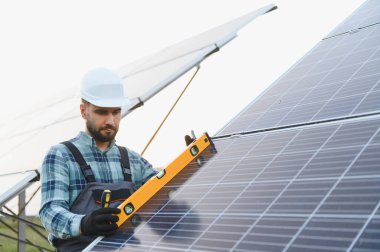 Sert şapka ve koruyucu tulum giyen mühendis yenilenebilir enerji üretimi için yeni bir güneş paneli sistemi kuruyor