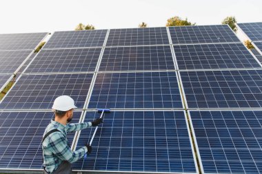 Güneş panellerini temizleyen, yenilenebilir enerji üretimi için optimal performans sağlayan, kalın şapka ve eldiven giyen işçiler