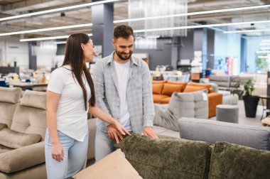 Çift evleri için yeni bir kanepe seçiyor, modern mobilya galerisinde kumaşa dokunuyor, satın alma kararı veriyor.