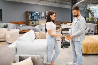 Genç bir çift mobilya mağazasında kumaş örneklerini karşılaştırıyor, yeni evleri için döşeme yapmaya karar veriyorlar, mobilya alıyorlar.