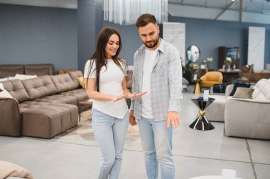 Parlak mobilya galerisinde modern koltukları karşılaştıran bir çift, yeni evleri için şık bir kanepe seçerken gülümsüyorlar - 120 çar. - 