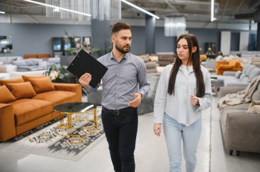 Satış danışmanı bayan bir müşteriyle iletişim kuruyor, seçenekleri tartışıyor ve modern bir mobilya mağazasında onun satın alma kararlarını almasına yardım ediyor.