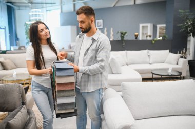Yeni evleri için döşeme kumaşı örnekleri seçen genç bir çift modern bir mobilya galerisinde karar veriyor.