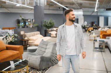 Mutlu adam alışveriş yapıyor ve modern bir mobilya mağazasında yeni ev dekorasyonu seçiyor. Gülümseyerek etrafa bakıyor.