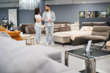 Genç çift modern bir mobilya mağazasında alışverişleri tartışıyor, ev dekorasyonu ve iç tasarım için eşyalar seçiyor.