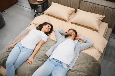 Mutlu genç çift bir yatakta uzanıyor, gülümsüyor ve birbirlerine bakıyor, ev için mobilyaları seçerken bir anın tadını çıkarıyorlar.