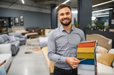 Sırıtkan satış danışmanı elinde kumaş örnekleri, yeni mobilyalar için malzeme seçen bir kadına yardım ediyor.