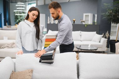 Modern mobilya mağazasında bir satış danışmanıyla kanepe döşemelerine bakan kadın müşteri.