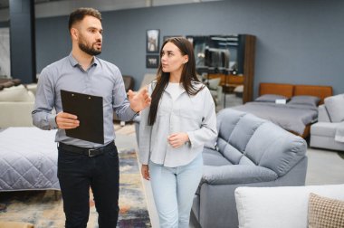 Kadın müşteriye ürün özelliklerini açıklayan erkek satış danışmanı modern bir galeride mobilya alışverişi yapıyor.