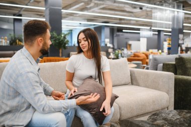 Bir çift kanepede otururken tartışıyor, perakende satış mağazasında evleri için yeni mobilyalar seçiyor.