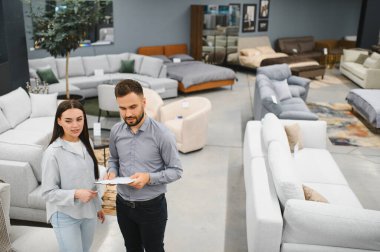 Female customer consults with sales assistant while browsing modern furniture showroom, discussing options for new home comfort and design