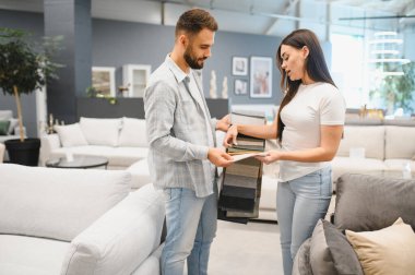 Young couple comparing upholstery swatches, making a decision on new furniture fabric, shopping in a modern retail store