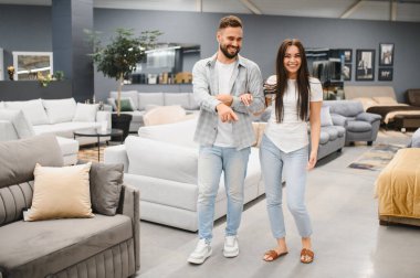 Young couple happily choosing a modern sofa in a furniture showroom while planning and furnishing their new apartment together