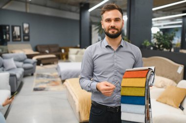 Man sales consultant holding various fabric samples, offering choices for customers in a modern furniture store setting