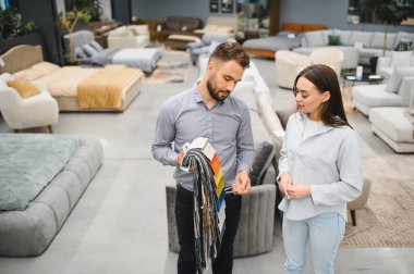 Sales consultant showing fabric samples to a potential female buyer while shopping for new furniture in a modern store