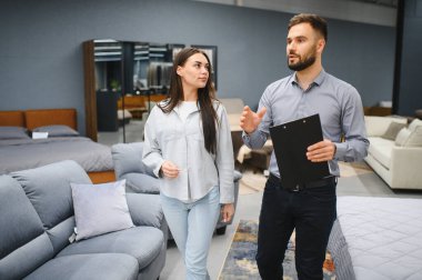 Couple consults with sales rep in modern furniture showroom, discussing options and choosing new sofa and home decor pieces