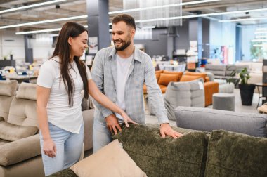 Happy couple touching sofa fabric in a furniture showroom. They are making decisions for furnishing a new home