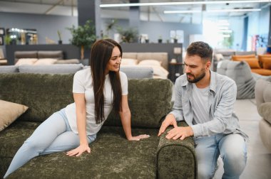 Young couple selecting a new sofa in a modern showroom, discussing options and testing comfort for their future home and lifestyle plans