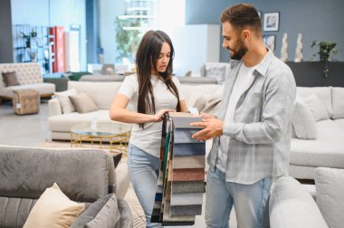 Happy couple selecting upholstery material samples, planning home decor in a sofa and furniture store