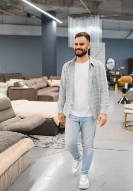 Young man smiling and walking through a modern furniture store showroom, shopping for home decor and furnishings