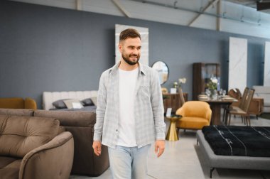 Man smiling while walking through a large modern furniture store, looking for interior design ideas for his apartment