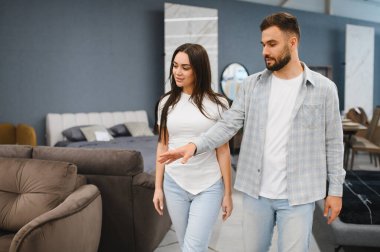 Young couple looking at a sofa in a modern furniture store showroom, selecting new home furnishings together