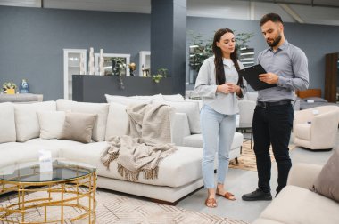 Woman and sales consultant discussing sofa purchase in a modern furniture store, offering customer service and retail assistance