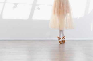 Balerin kız bacakları, bale ayakkabıları ve beyaz duvarlı dans okulunda bale eğitimi alan etek.