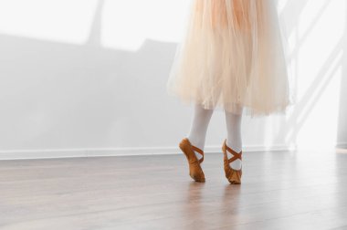 Genç balerin bir dans stüdyosunda bale yapıyor, etek ve kahverengi noktalı ayakkabı giyiyor, zarafet ve adanmışlık sergiliyor.