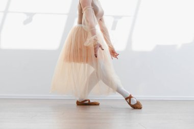 Balerin, parlak bir dans stüdyosunda bej etek ve kahverengi dans ayakkabıları giyerek bale dansına hazırlanıyor.