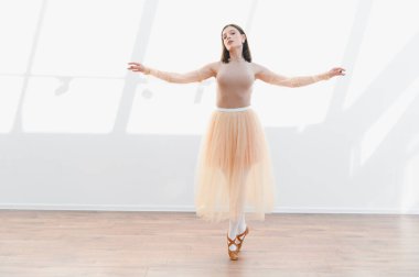 Genç balerin, bir dans stüdyosunda bale yapıyor. Doğal ışıkla aydınlatılıyor. Zarafet ve duruş sergiliyor.