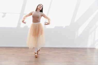 Genç balerin zarif dans hareketlerini parlak bir stüdyoda yapıyor, zarafetini ve duruşunu sergiliyor.