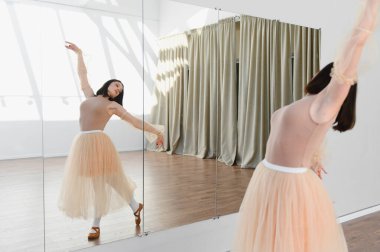 Genç balerin dans stüdyosunda bale çalışıyor. Aynayı kullanarak duruşunu ve tekniğini mükemmelleştiriyor.